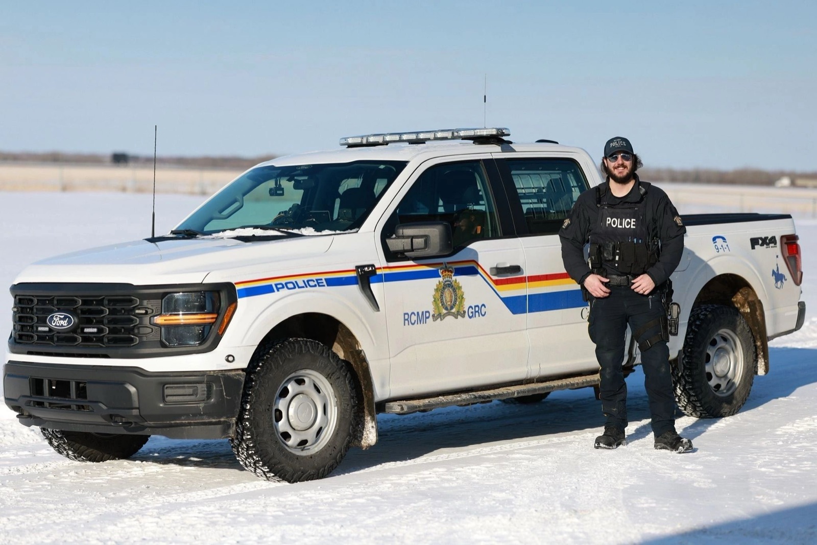 A police officer in uniform beside an RCMP patrol truck in winter